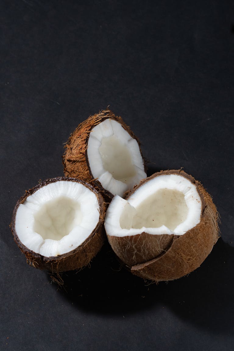Three freshly opened coconuts displayed on a dark backdrop showcasing fresh white coconut flesh.
