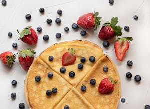 Mouth-watering crepes topped with fresh strawberries and blueberries on a white table.