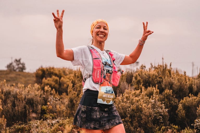 Smiling female athlete on a nature trail, celebrating with peace signs.