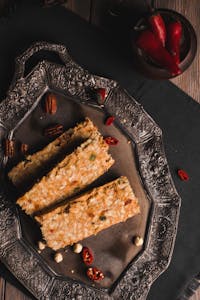Three oat bars arranged on an ornate tray with pecans and chili peppers.
