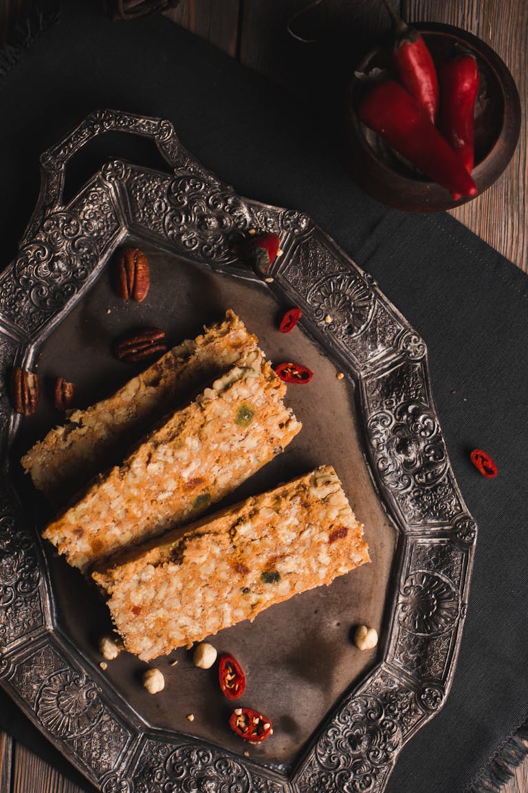 Three oat bars arranged on an ornate tray with pecans and chili peppers.