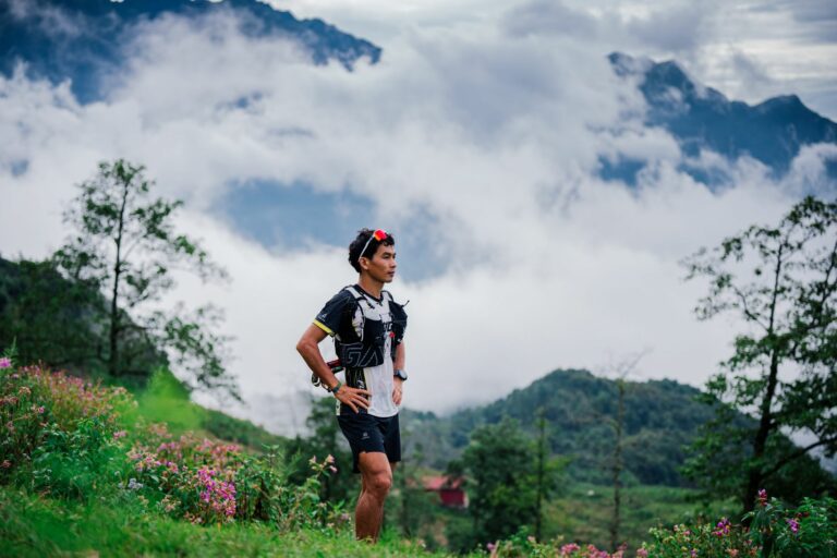 Traileur assis en montagne après une course d’été, récupérant au calme avec ses chaussures de trail et une gourde.
